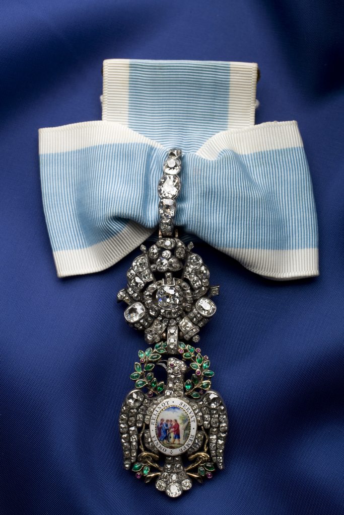 Front side of the gold and silver insignia of the Society of the Cincinnati adorned with gemstones hanging from a blue-and-white silk ribbon