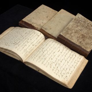 Four manuscript orderly books from the Revolutionary War, one open with handwriting filling the pages and three others closed beside it