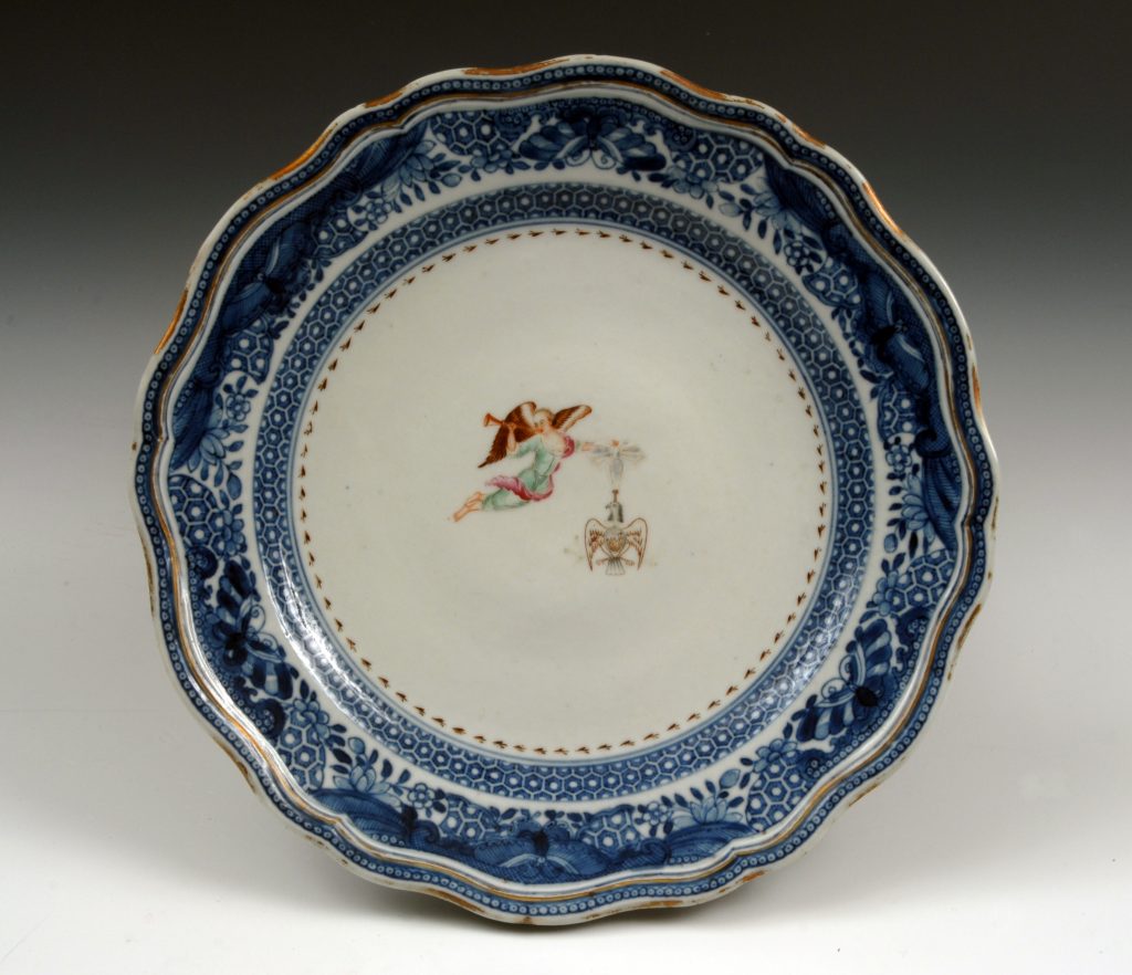 Circular porcelain plate with a blue border and white center decorated with a winged figure holding an Eagle insignia