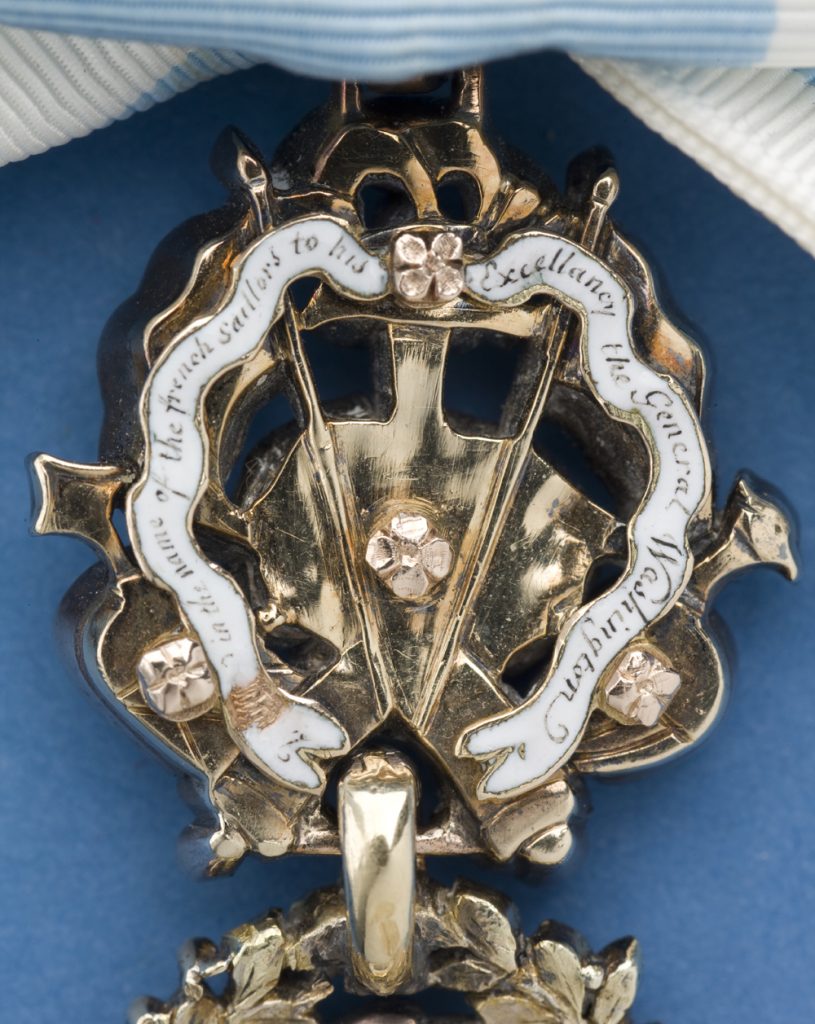 Back side of the gold trophy of a medal with an inscription on a white enamel ribbon