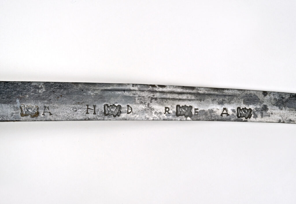 Detail of a slightly curved sword blade showing stamped letters and marks