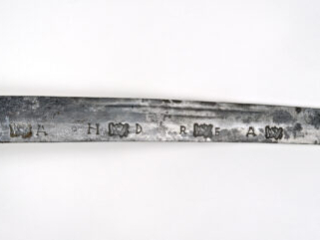 Detail of a slightly curved sword blade showing stamped letters and marks