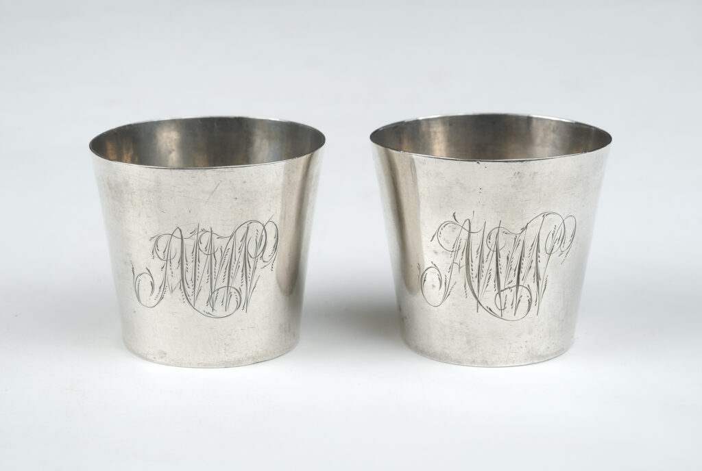 Two identical silver camp cups with initials engraved on the front